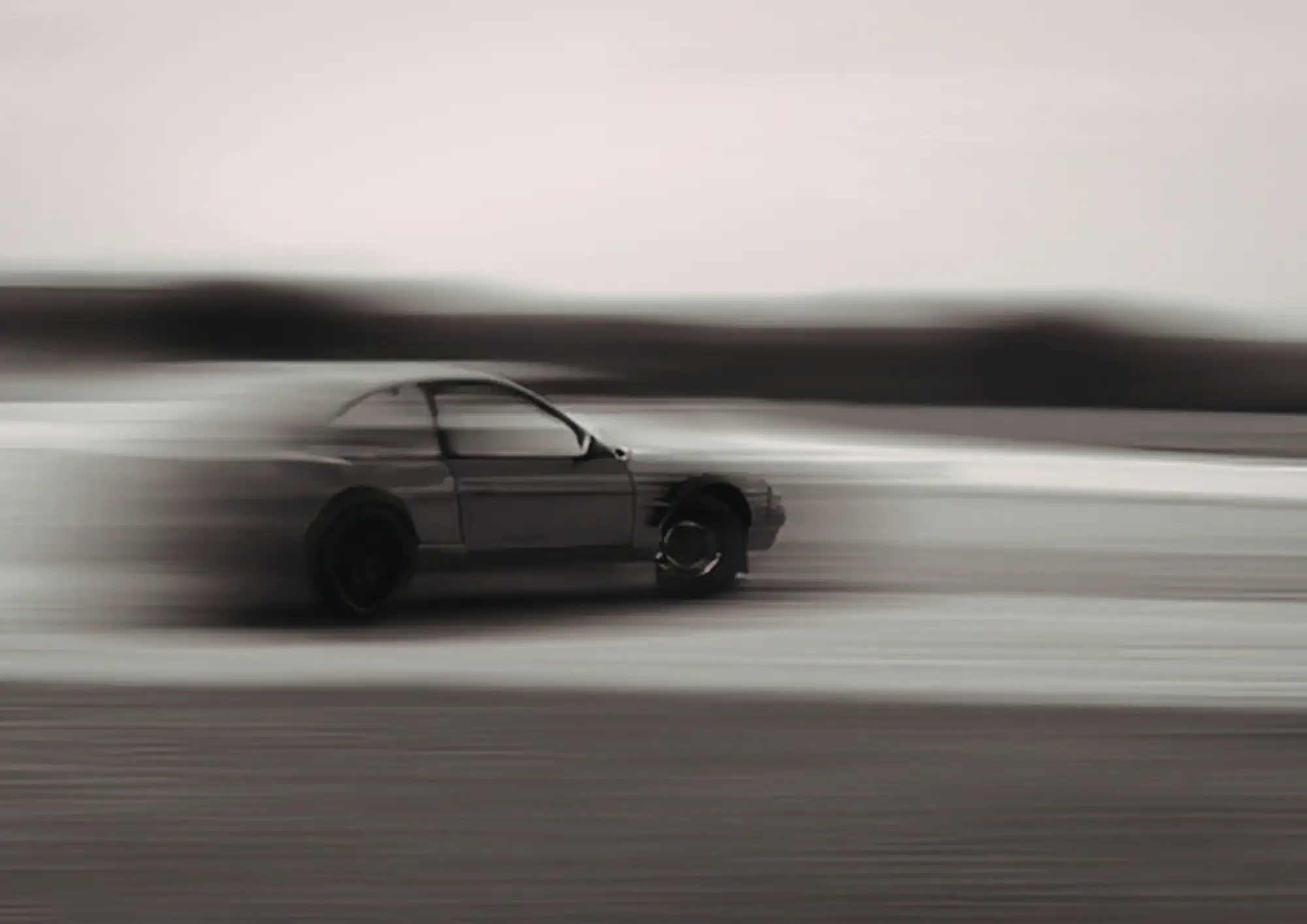 A car photographed mid-corner in monochrome, panned so the car is sharp and the road and horizon are pulled into horizontal streaks.